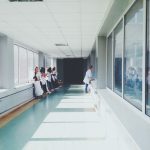 Corredor de hospital bem iluminado, com profissionais de saúde usando jalecos brancos.