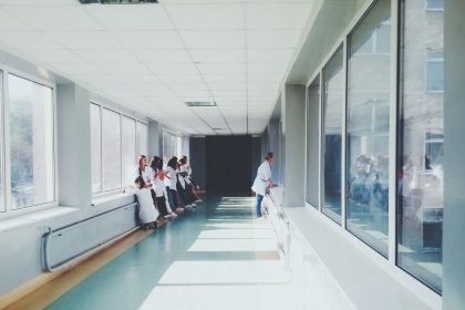 Corredor de hospital bem iluminado, com profissionais de saúde usando jalecos brancos.