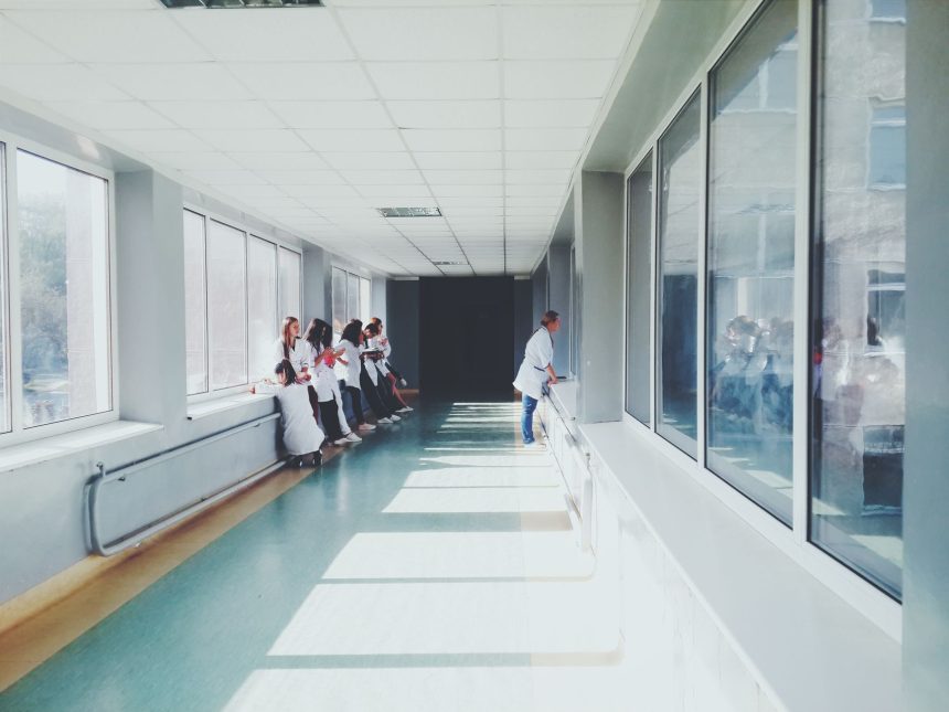 Corredor de hospital bem iluminado, com profissionais de saúde usando jalecos brancos.